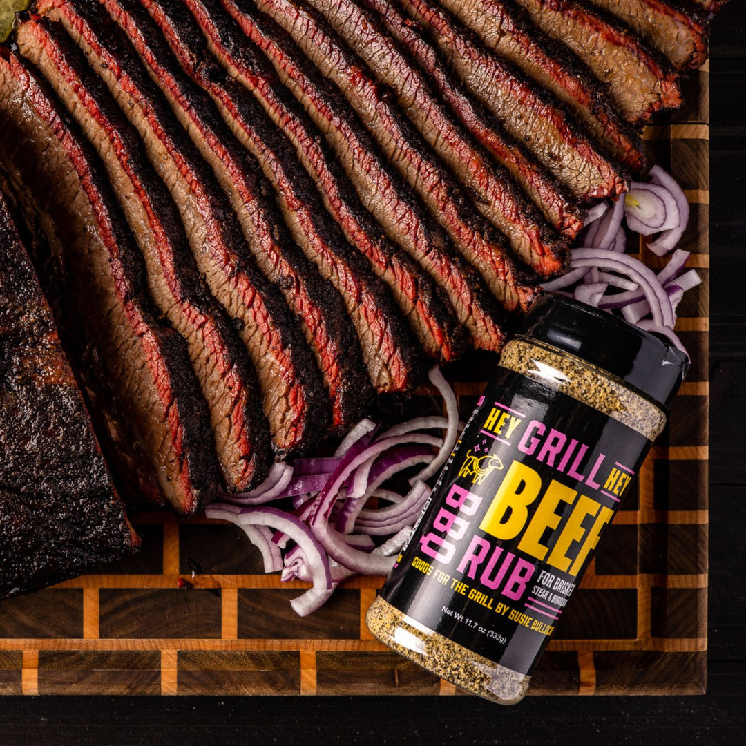 Sliced beef brisket sits on a cutting board next to sliced onions and a bottle of beef rub. 